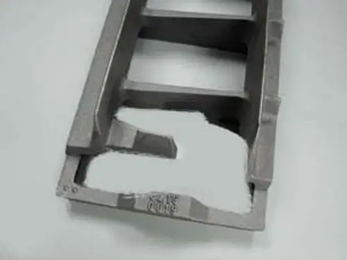 Graue Metallform mit mehreren Aussparungen und strukturierten Oberflächen, möglicherweise Teil eines Heizsystems von Remeha.